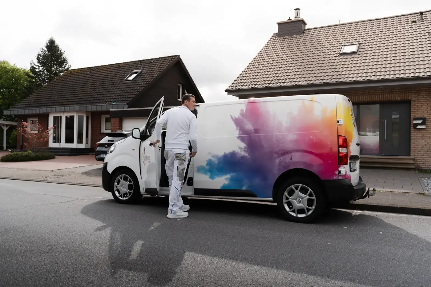 Maler steigt in den bunt beklebten Firmenwagen